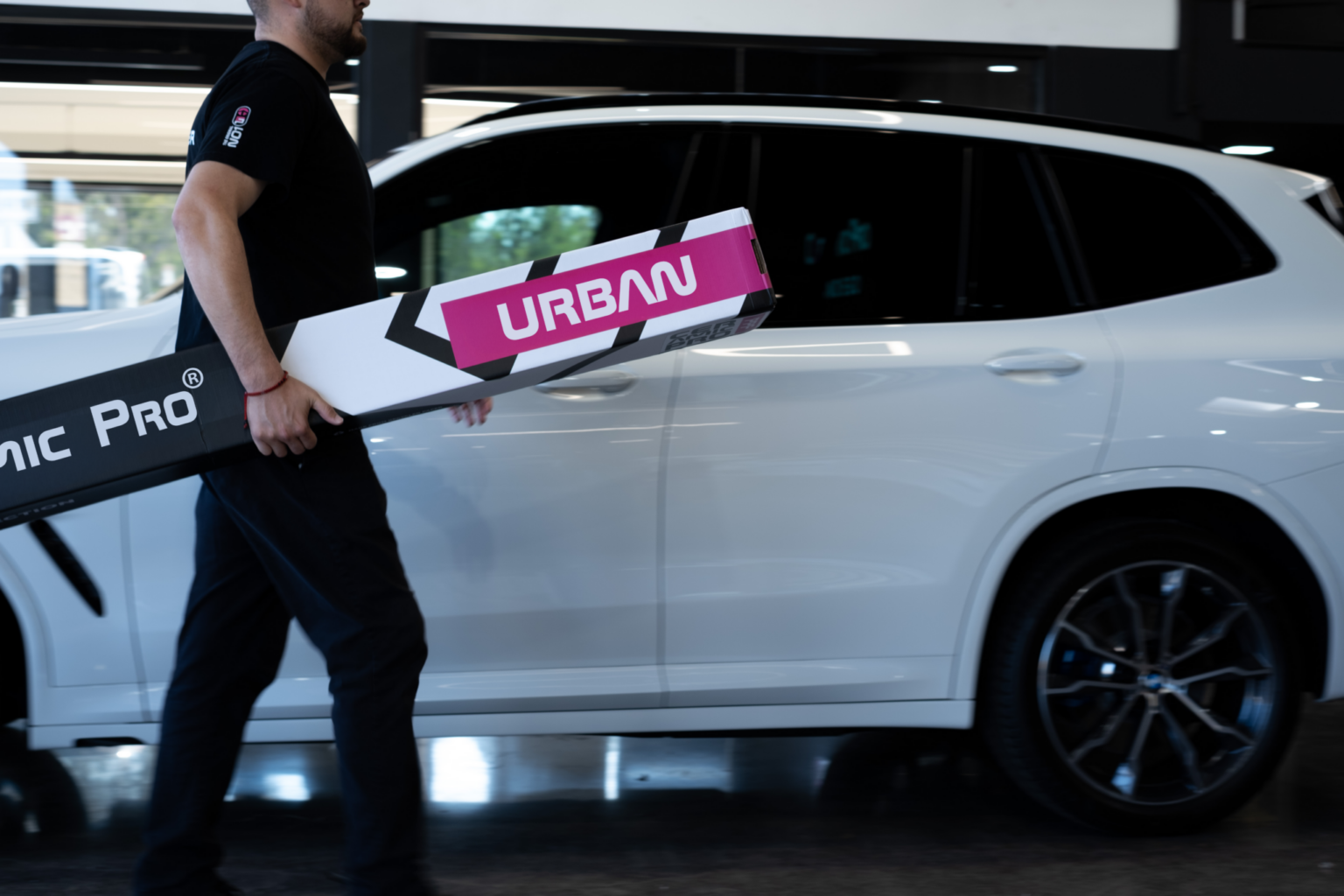 Person carrying equipment beside white car.