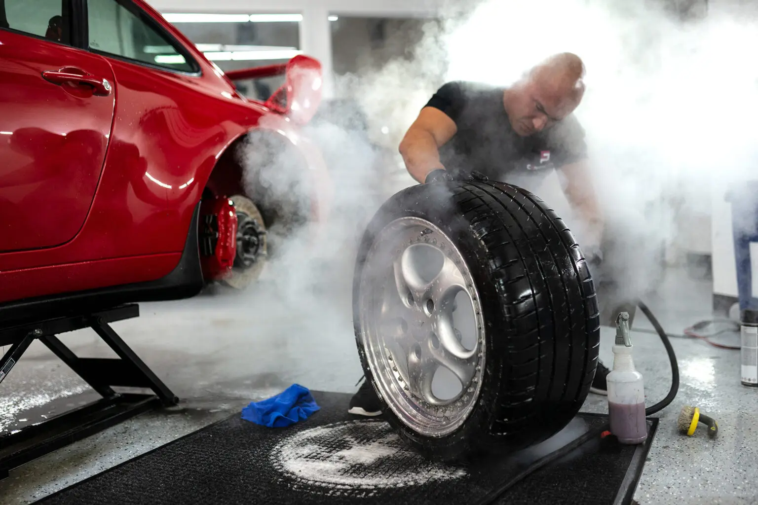 Man cleaning tire near red car lift.