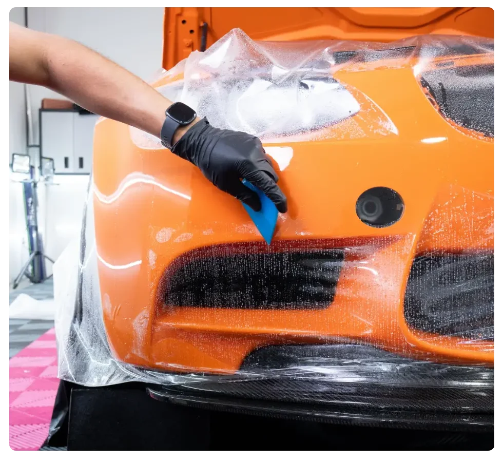 Applying protective film to orange car.